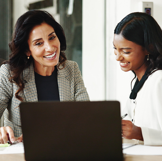 two woman looking at laptop and writing notes